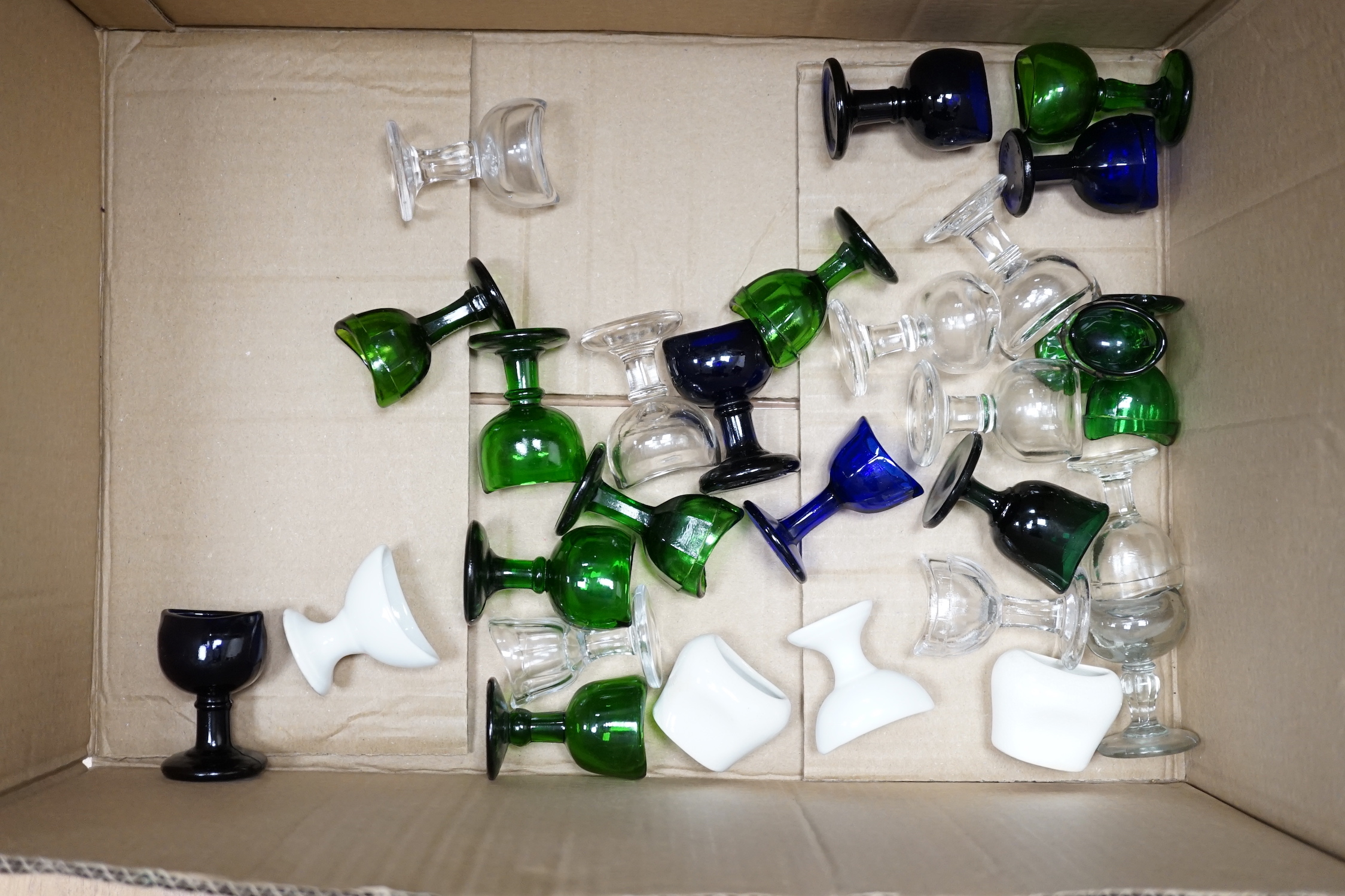 Thirty-four glass and porcelain eye baths, including green and blue glass examples